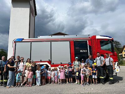 Feuerwehrleute und Kinder posieren vor einem roten Löschfahrzeug in Österreich