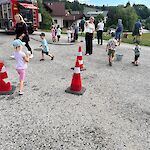 Feuerwehrübung mit Kindern in Oberösterreich, mehrere Kinder laufen mit Eimern und Hütchen auf einem Schotterplatz.