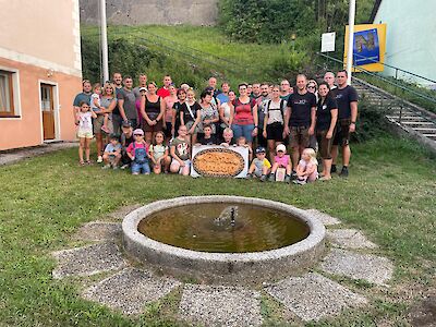 Gruppe von Erwachsenen und Kindern steht vor einem Haus in Österreich mit einem Brunnen im Vordergrund.
